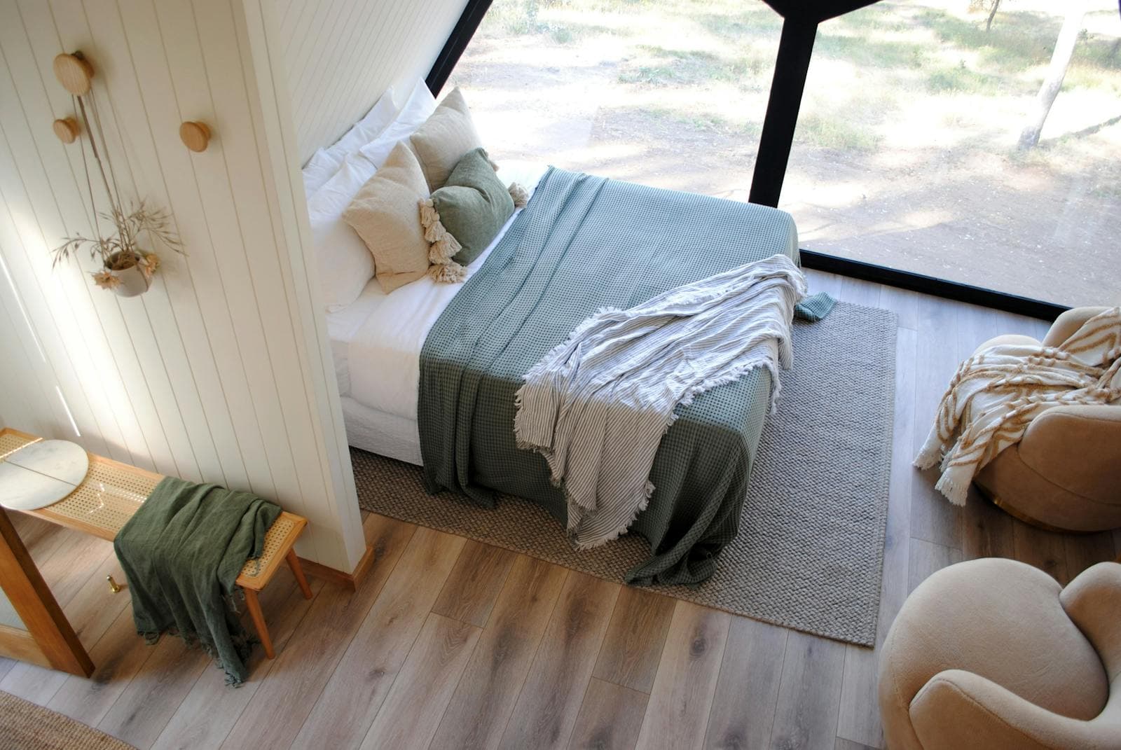 The queen bed beside the cabin's full-height window, a sage throw folded on top