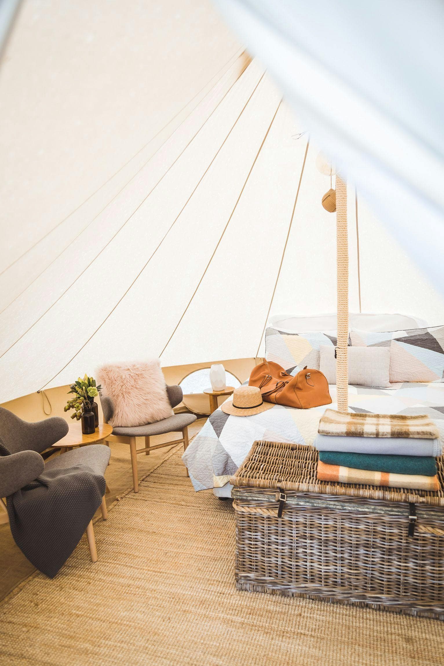 Inside a Classic bell tent: the grey lounge, cushions and the queen bed under the canvas peak